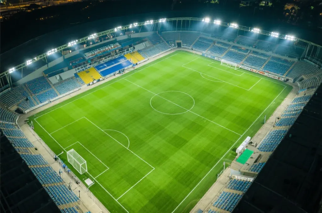 An aerial view of a modern soccer stadium field under bright floodlights, lush green grass, no people, wide angle